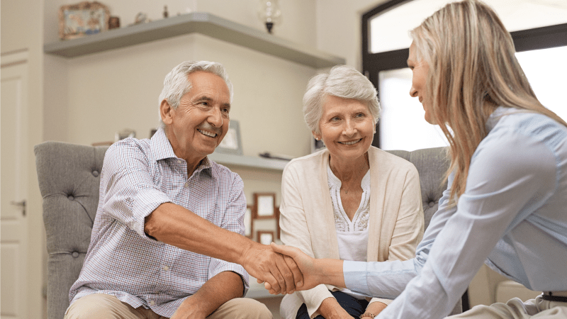 Smiling elderly couple meeting with advisor, shaking hands warmly.