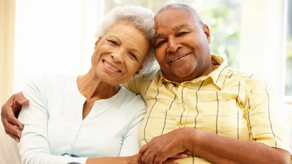 Happy elderly couple hugging closely, smiling warmly at camera.