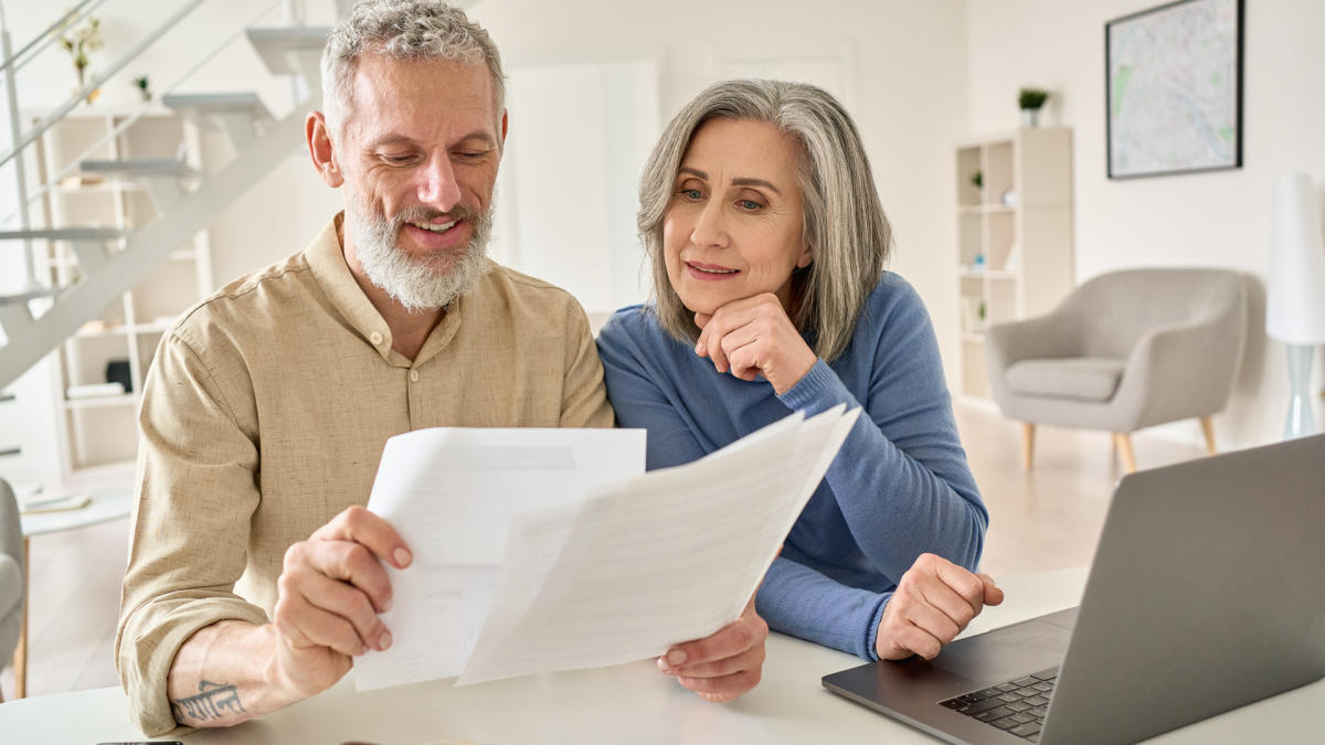 Smiling older couple reviewing documents together near laptop at home.