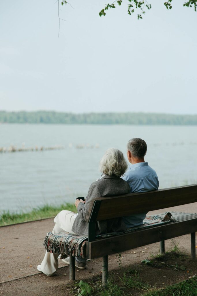 Older couple sitting together on bench, gazing out at lake.