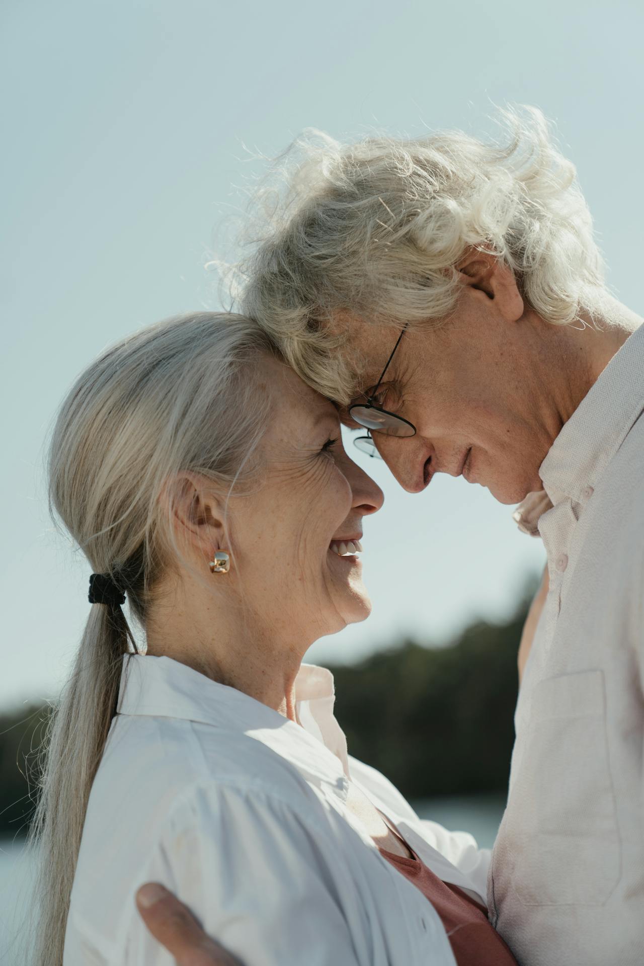 Smiling elderly couple embracing closely, foreheads touching lovingly.
