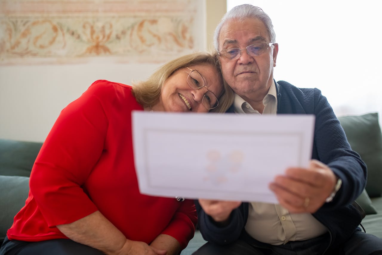 Elderly couple sitting close, looking at a paper with smiles.