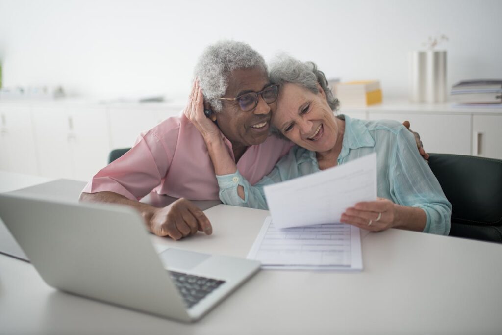 Happy elderly couple hugging while reading document near laptop.
