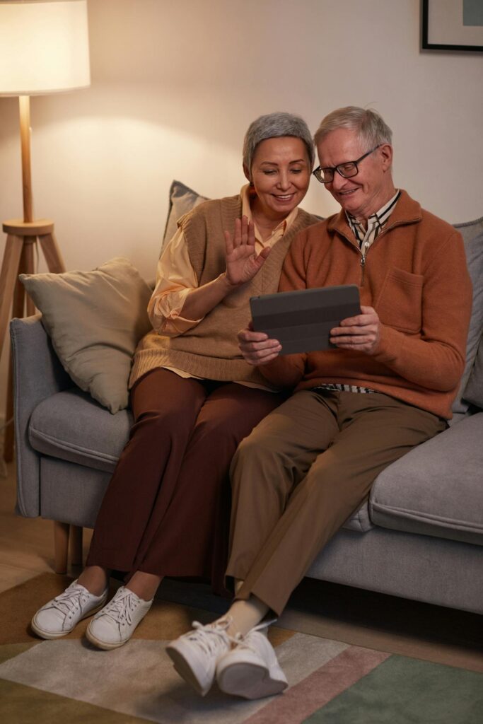 Older couple sitting on couch, video calling on a tablet device.
