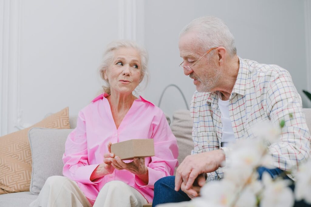 Older woman in pink blouse giving gift box to partner.
