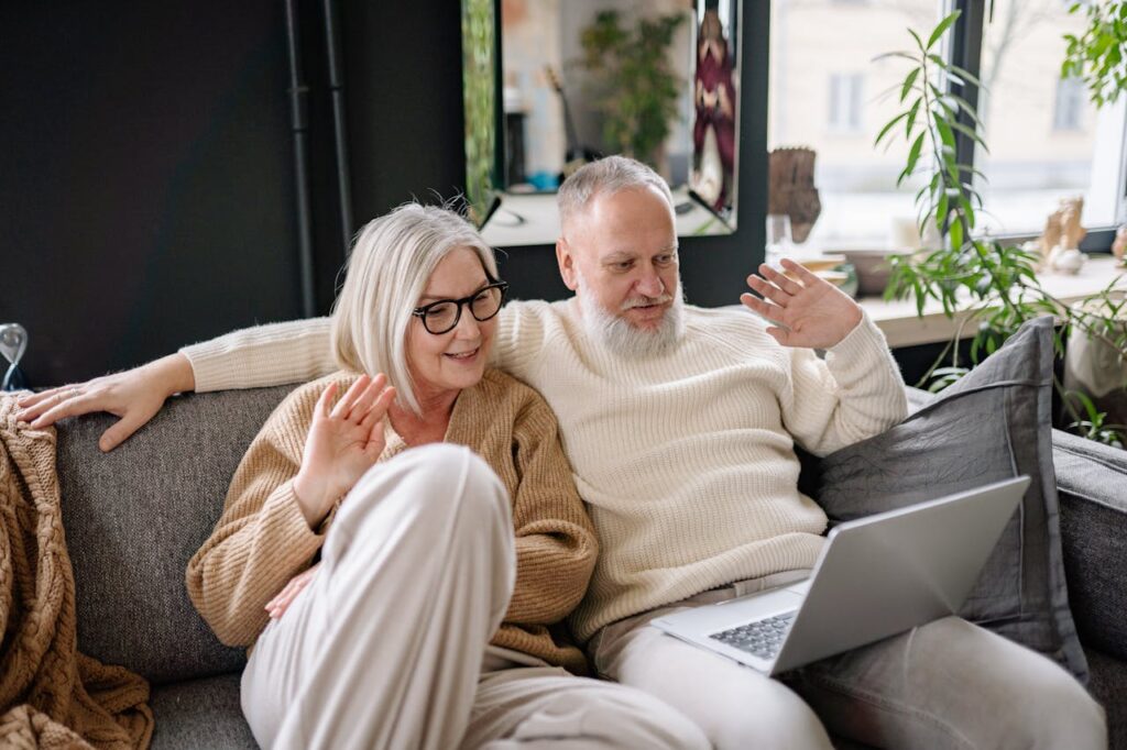Older couple sitting on couch, waving happily during a video call.