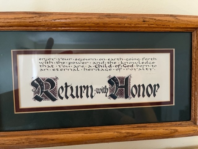 Framed wall art with text reading "Return with Honor" in calligraphy.