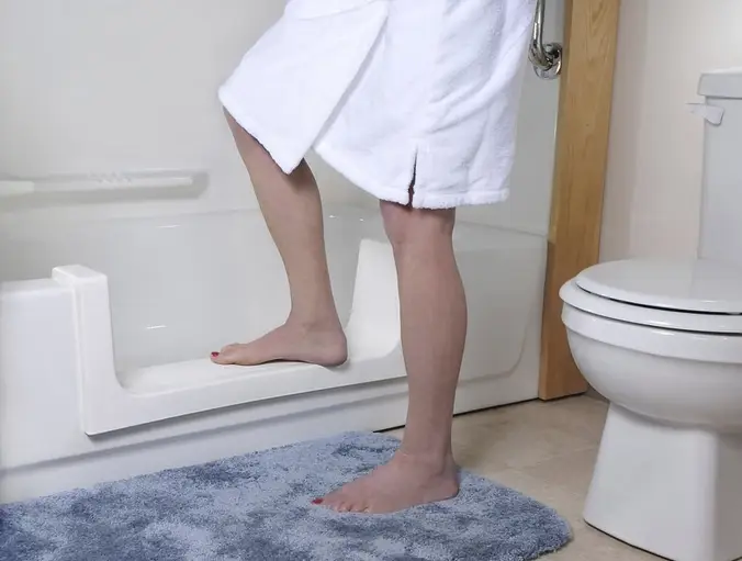 Person stepping into bathtub using a white safety step near toilet.