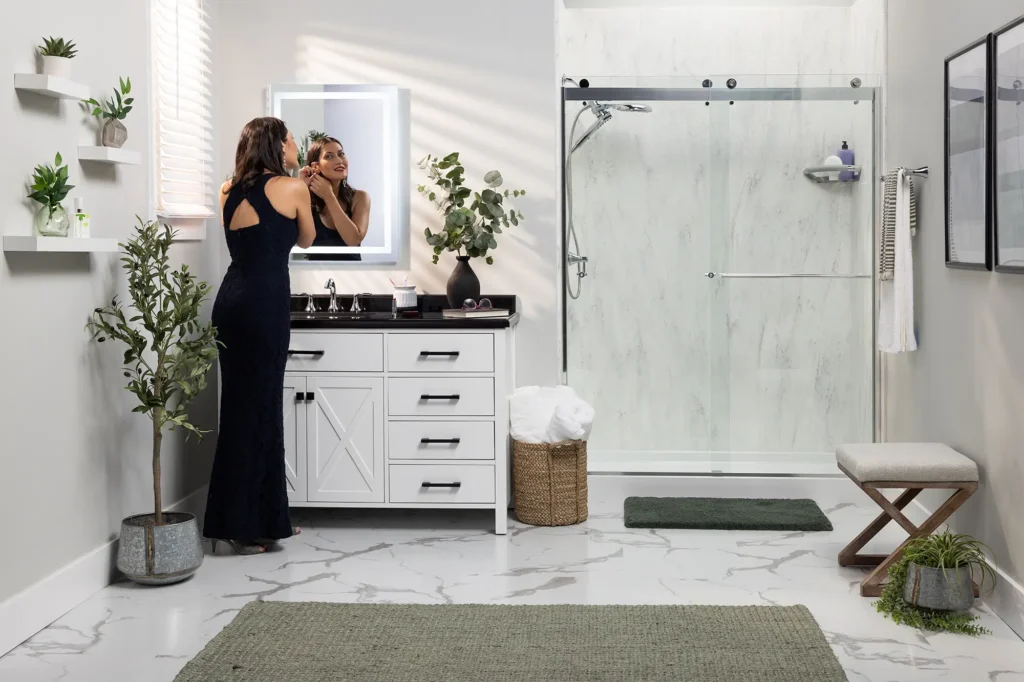 Woman standing beside white bathroom vanity and spacious glass walk-in shower.